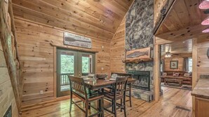 A wooden interior with a stone fireplace, a dining area with a table and chairs, and a sign above the door. - Hemptown Hideway (Mineral Bluff)