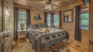 A wooden cabin bedroom with a bed, a ceiling fan, and a large window. - Hemptown Hideway (Mineral Bluff)