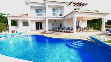 A two-story house with a swimming pool, outdoor seating, and a pergola.