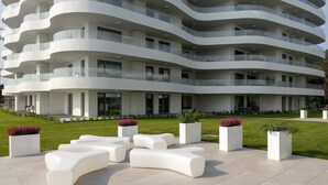 Un edificio moderno de varios pisos con fachada curva, zonas de estar al aire libre y un césped cuidado.