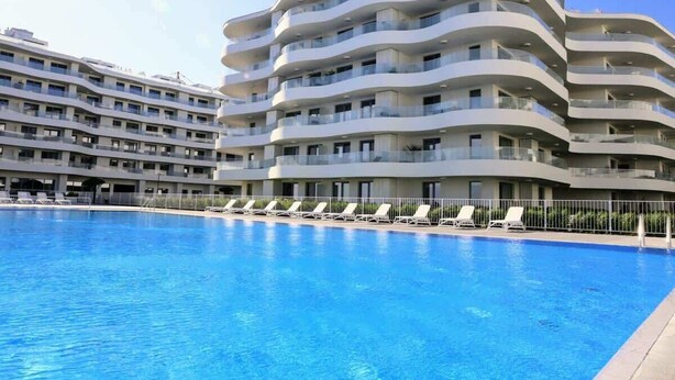 Un hotel moderno con zona de piscina, que presenta un edificio curvo con varios balcones y una piscina azul cristalina.