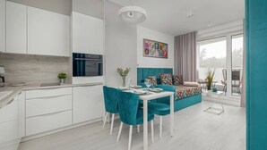 Una cocina moderna con armarios blancos, una mesa de comedor con sillas turquesa y un sofá colorido con cojines estampados.