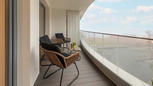 A balcony with wicker furniture, a glass railing, and a view of the sky and distant landscape. - Stylish Apartment | Parking, Balcony, Close to the Beach (Rogowo)