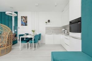 A modern kitchen with white cabinets, a black microwave, and a dining area with teal chairs and a white table.