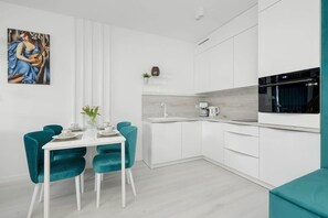 A modern kitchen with white cabinets, a dining table with teal chairs, and a painting on the wall.