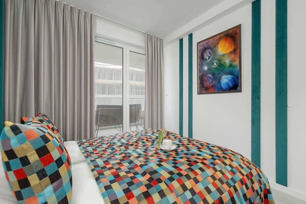 Una habitación de hotel con una colcha a cuadros, un cuadro de planetas y vistas a través de un ventanal grande.