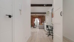 Un pasillo que conduce a una sala de estar con pared de ladrillo, un sofá, una mesa y una planta colgante.