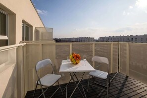 Un balcon avec une table et des chaises, un panier de fruits et une vue sur la ville.