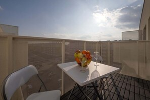 Un balcon avec une table, des chaises, un panier de fruits et des verres à vin.