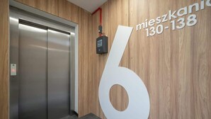 Un elevador moderno con un panel de control y una pared de madera que tiene un número '6' blanco grande y un número de teléfono.
