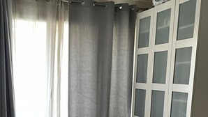 Un dormitorio con cama, una silla de madera, un ventilador de pie y un armario con puertas de vidrio esmerilado.