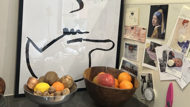 Un comptoir de cuisine orné d’une œuvre d’art abstraite encadrée, un saladier rempli de fruits, un bol en métal contenant des noix et une paire de ciseaux roses.