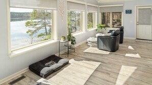 A spacious room with large windows overlooking a lake, a ceiling fan, and a seating area with a massage chair. - Dreamcatcher On Lake Coronado (Hot Springs Village)
