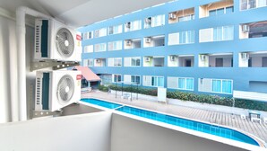 Un balcón de hotel con piscina, unidades de aire acondicionado y vistas de un edificio azul con varios balcones.