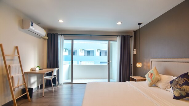 Habitación de hotel con cama, escritorio, silla, escalera y vistas a edificios a través de un ventanal amplio.