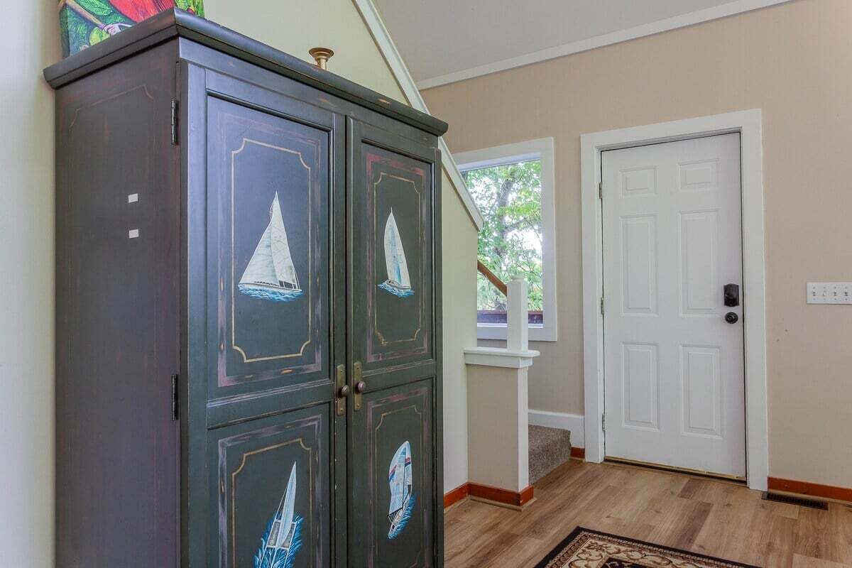 A hallway with a dark wooden cabinet with sailboat paintings, a white door, and a wooden floor.