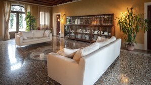 A spacious living room with a white sofa, a glass cabinet with dishes, and a large potted plant.