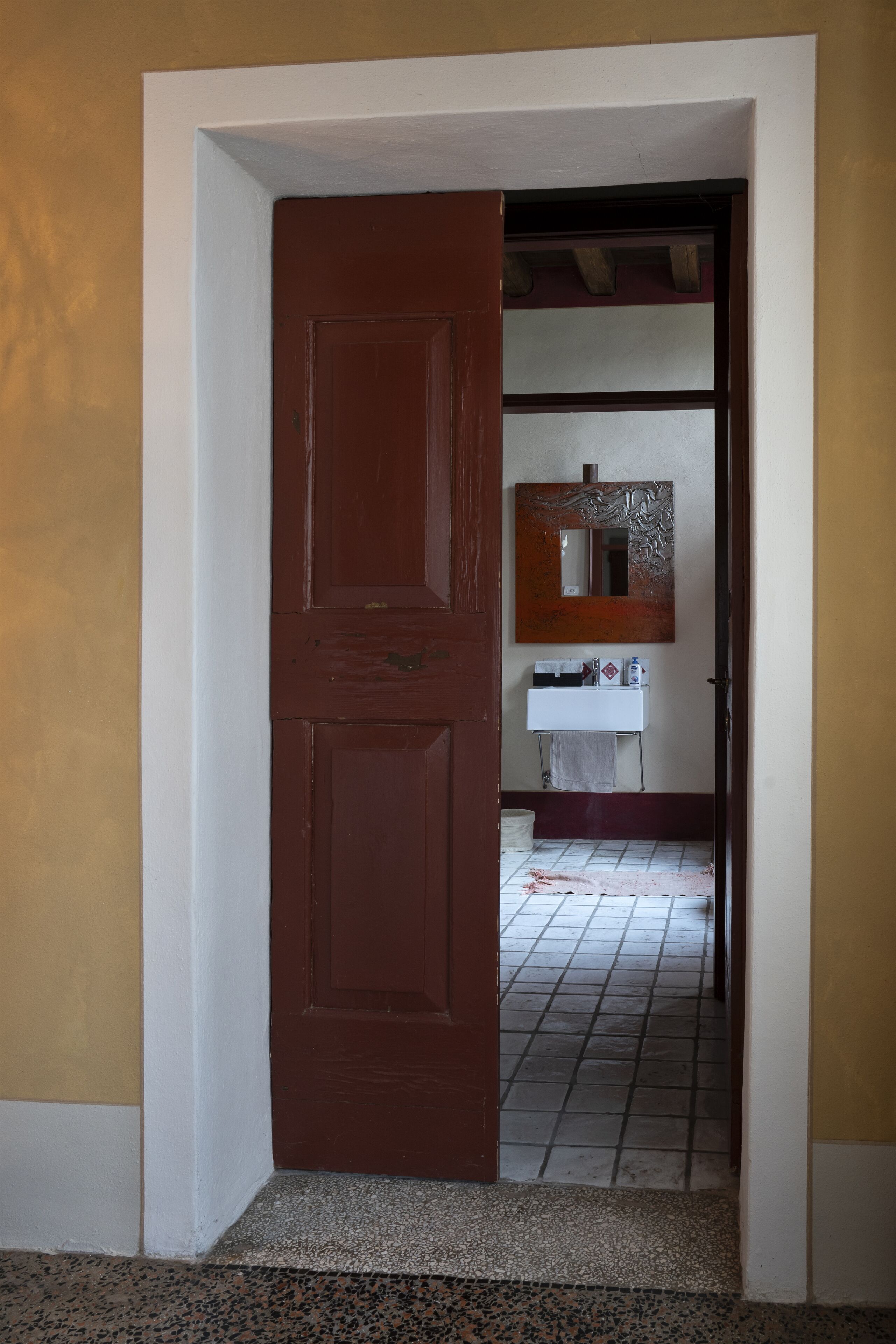Een deuropening naar een badkamer met een betegelde vloer, een wastafel en een spiegel.