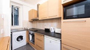 A compact kitchen with a washing machine, dishwasher, microwave, and a small countertop with a kettle and toaster. - Flat 1 Greek Street Apartments

 (London)