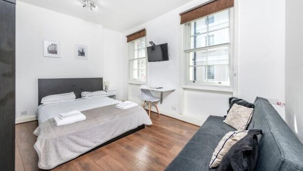 A modern hotel room with a large bed, a desk, a chair, and a sofa. - Flat 1 Greek Street Apartments

 (London)