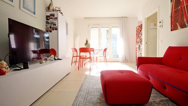 A modern living room with a red sofa, a flat-screen TV, and a dining area with red chairs. - Stunning 1-bed Apartment in Verona (Verona)