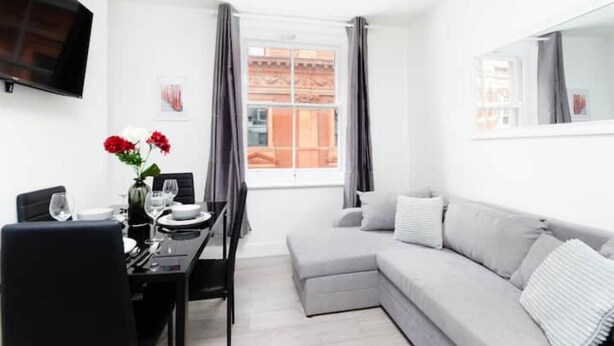 A modern living room with a grey sofa, a dining table with chairs, and a TV mounted on the wall. - Flat 2 Covent Garden Apartments

 (London)