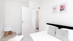 A modern hotel room with a large bed, a bedside table, a chair, and a door leading to another room. - Flat 2 Covent Garden Apartments

 (London)