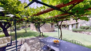 A patio with a table and chairs, a stone wall, and a pergola with vines. - Abejas 2 El Vergel de Chilla (Candeleda)