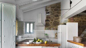 A kitchen with a stone wall, a wooden countertop, and a white refrigerator. - Abejas 2 El Vergel de Chilla (Candeleda)