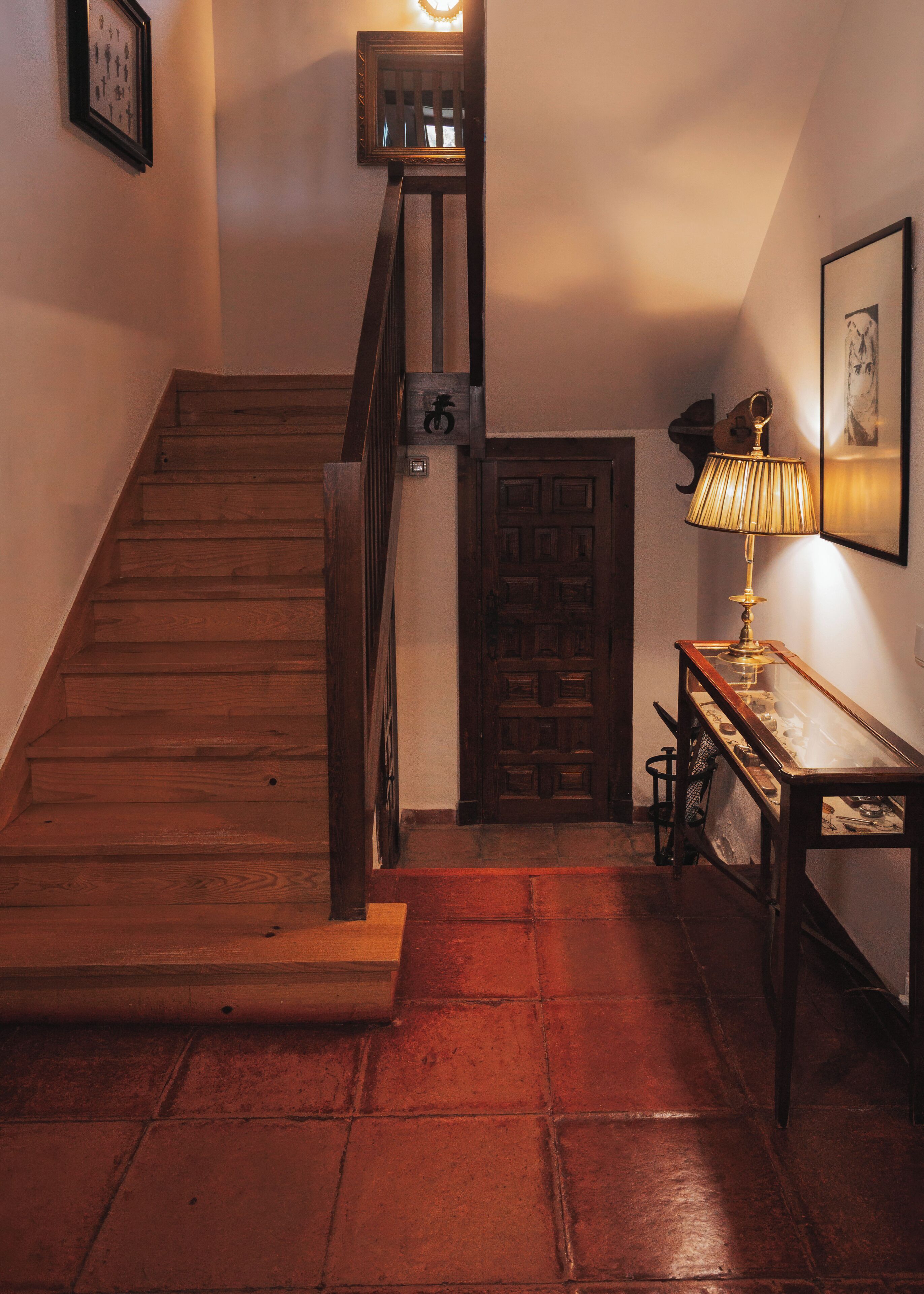 A wooden staircase with a handrail, a door with a traditional design, and a table with a lamp.
