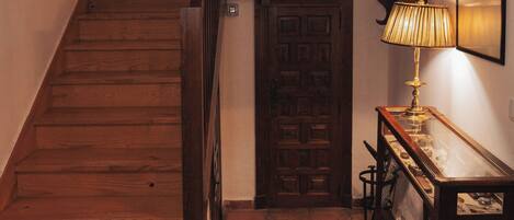 A wooden staircase with a handrail, a door with a traditional design, and a table with a lamp.