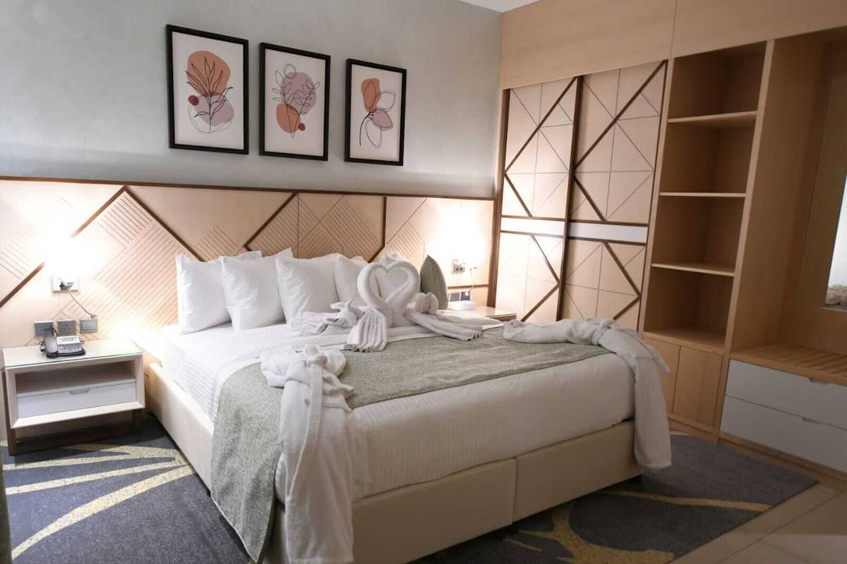Un lit bien fait, avec du linge de lit et des serviettes blanches, une table de chevet avec une lampe, et un mur orné de tableaux encadrés.