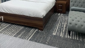 A modern bedroom with a wooden headboard, a large bed, a grey upholstered armchair, and a patterned rug. - LIA Hotel (Lungi)
