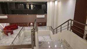A modern hotel lobby with a marble staircase, a red sofa, and a view of the city through large windows. - LIA Hotel (Lungi)