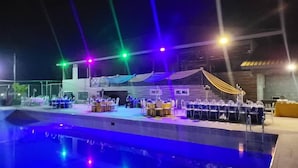 An outdoor event space with tables and chairs, a pool, and colorful stage lighting. - LIA Hotel (Lungi)
