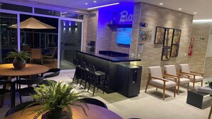 Zona de bar moderna con un letrero de neón, diferentes disposiciones de asientos y una pantalla de televisión.