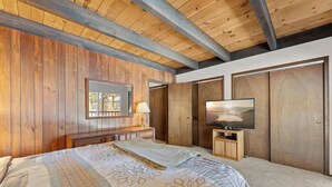 Ein Schlafzimmer mit Holzbalkendecke, einem Bett mit Blumenmuster-Bettwäsche, einem Fernseher und einem Kleiderschrank.