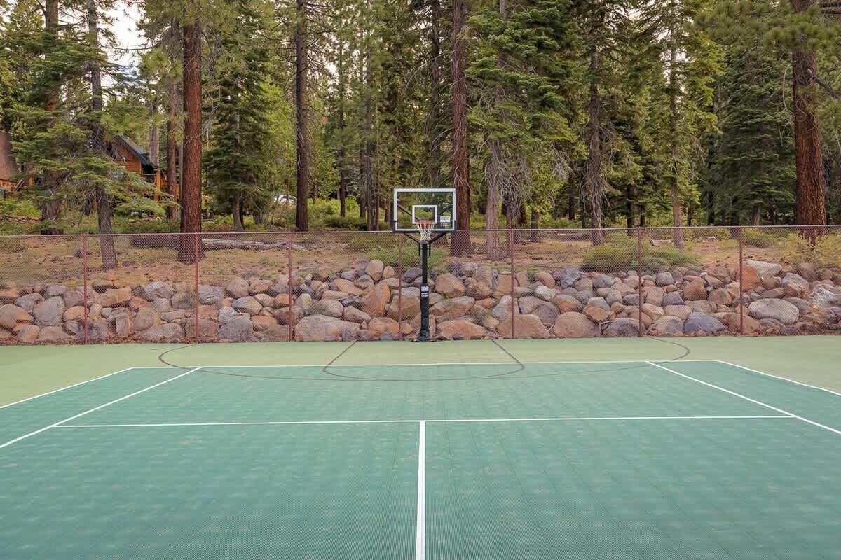 An outdoor basketball court surrounded by a stone wall and tall trees.