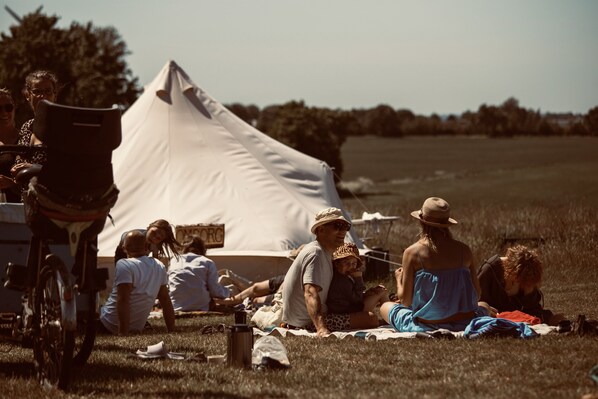 A group of people sitting on a blanket in a grassy field with a tent in the background.