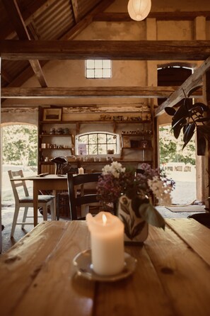 A rustic wooden interior with a table, chairs, a candle, and a vase of flowers.
