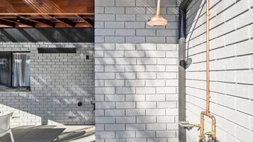 A modern outdoor shower with a copper showerhead, a brick wall, and a metal pipe system.