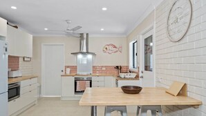 A modern kitchen with a central island, white cabinets, a stainless steel range hood, and a decorative fish wall art piece. - Sandy Shores Getaway (Mandurah)