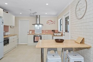 A modern kitchen with a central island, white cabinets, a stainless steel range hood, and a decorative fish wall art piece.