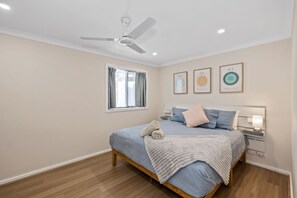A bedroom with a bed, a ceiling fan, a window with curtains, and wall art.