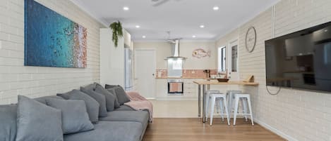 A modern living room with a grey sofa, a kitchen area with a TV, and a ceiling fan.
