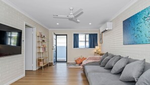 A modern living room with a grey sofa, a flat-screen TV, a ceiling fan, and a bookshelf. - Sandy Shores Getaway (Mandurah)