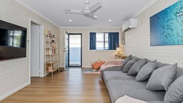 A modern living room with a grey sofa, a flat-screen TV, a ceiling fan, and a bookshelf.