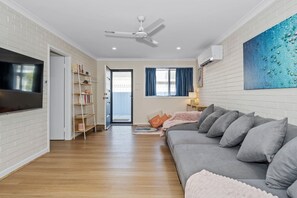 A modern living room with a grey sofa, a flat-screen TV, a ceiling fan, and a bookshelf.