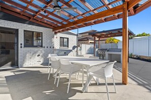 An outdoor patio with a covered seating area, a grill, and a white brick building in the background.