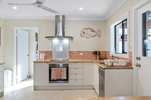 A modern kitchen with a central island, stainless steel range hood, and a window with a view. - Sandy Shores Getaway (Mandurah)